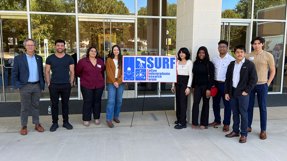 9 people standing next to a sign that reads socon undergraduate research forum