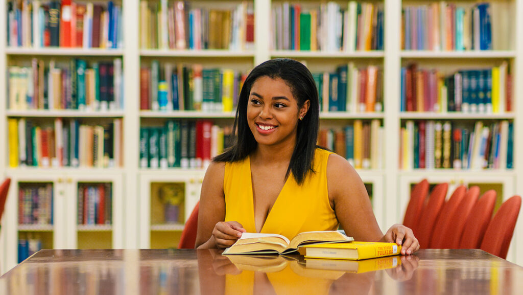 Student sits in a library looking at a book.