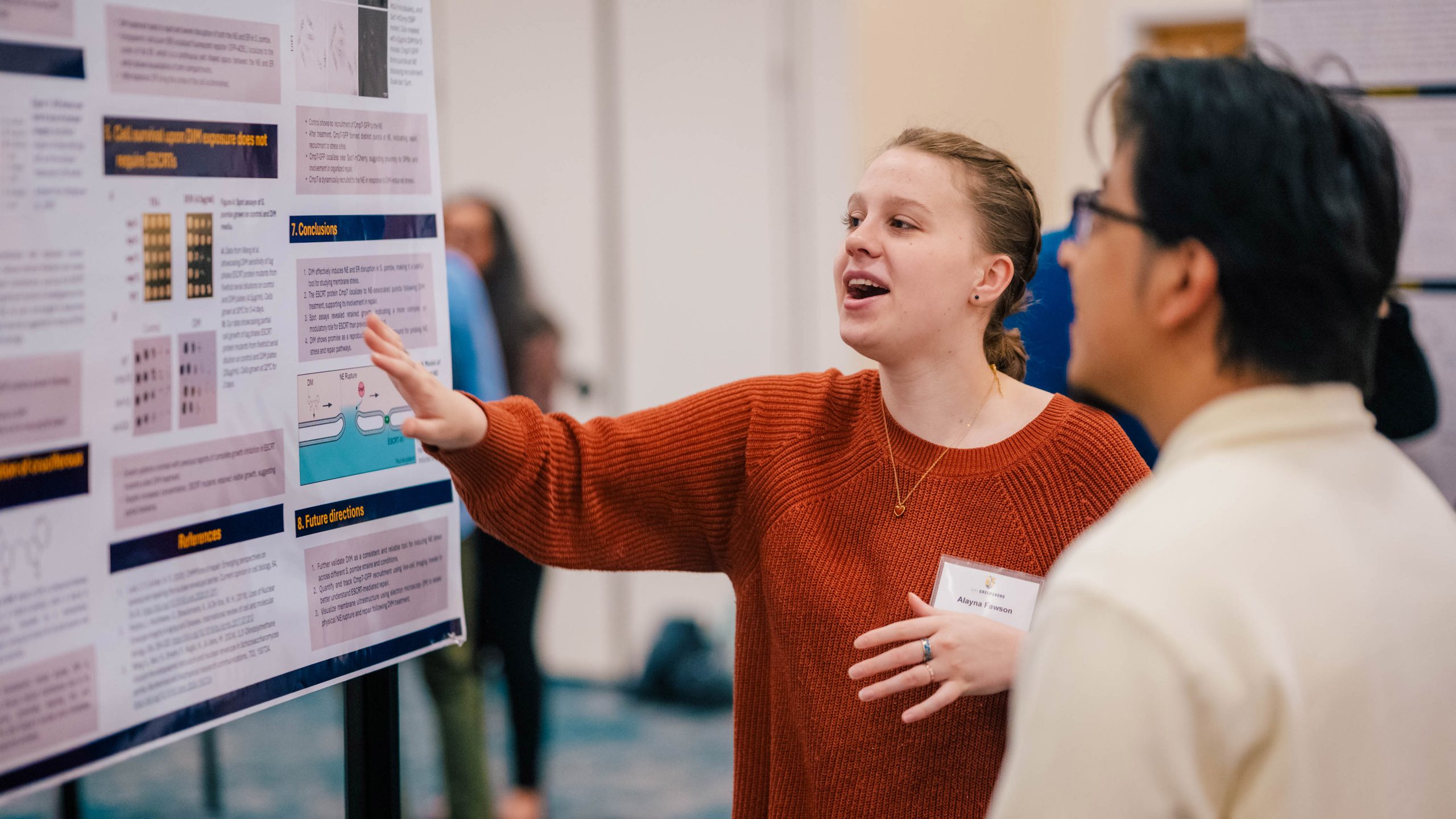 An animated student gestures to her poster as she explains her research to an expo attendee
